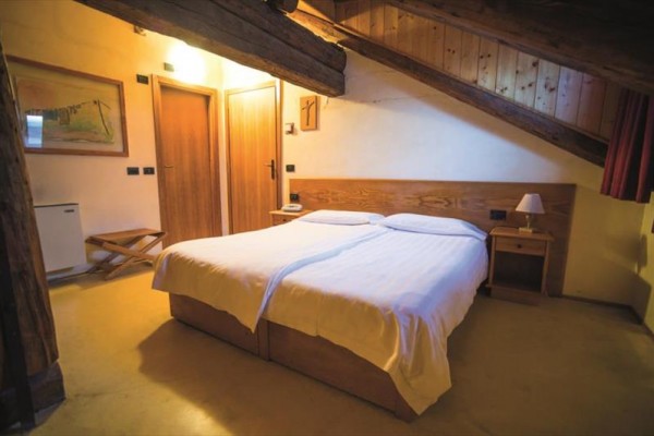 Pokoj s dvojlůžkem, dřevěnými trámy a nočními stolky pod šikmým stropem.