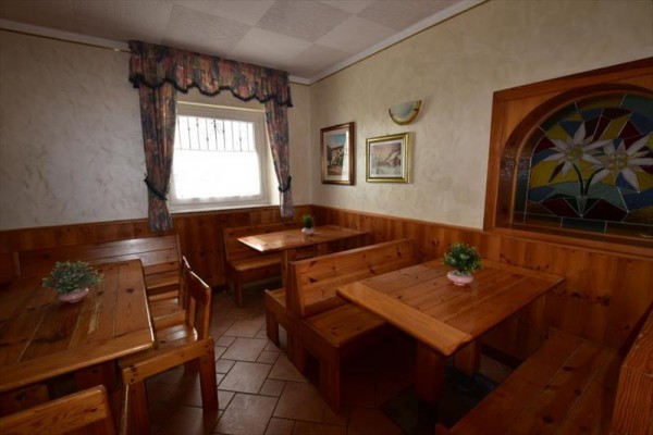 Dřevěný interiér s lavicemi, stolem a květinami, u okna s barevným sklem v pozadí.