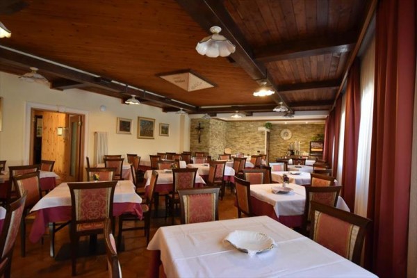 Restaurace s dřevěným stropem, prostřenými stoly a červenými závěsy.