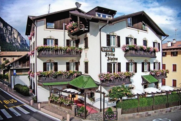 Tradiční hotel zdobený květinami s balkonem a terasou u hory.