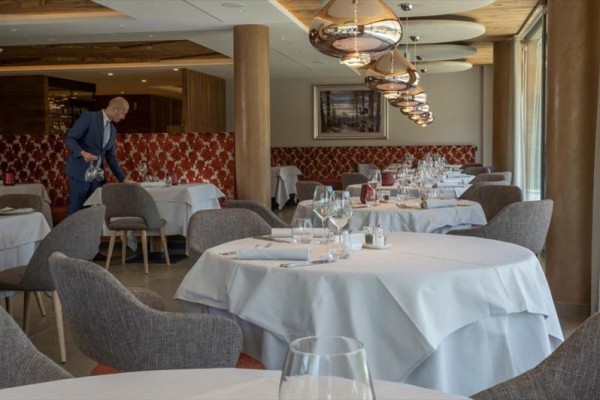 Luxusní restaurace s kulatými stoly a připraveným prostíráním, muž nalévá vodu.