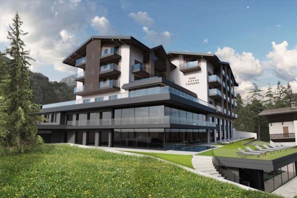 Moderní horský hotel s prosklenou fasádou obklopený lesy a loukou.
