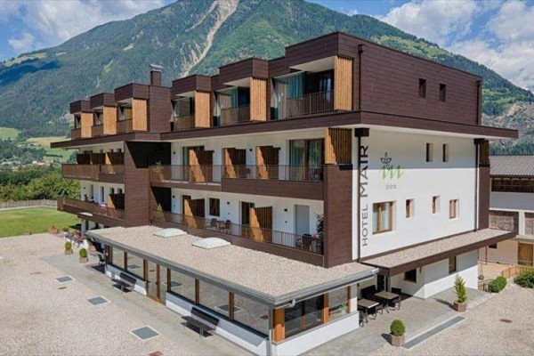 Moderní hotel s dřevěnými balkony na pozadí horského masivu.  