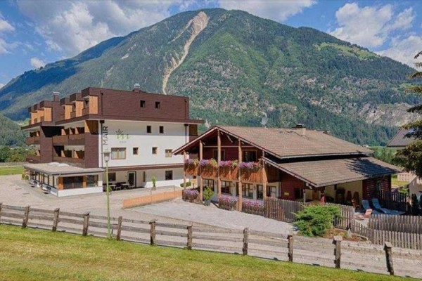 Horský hotel s dřevěnými balkony plnými květin na úpatí zelené hory.  
