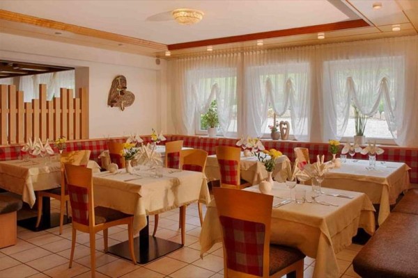 Elegantní restaurace s dřevěnými židlemi a prostřenými stoly u okna s květinami.