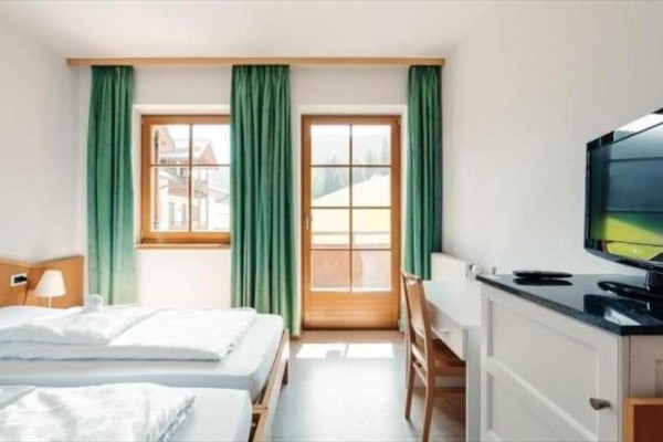 Světlý hotelový pokoj se dvěma lůžky, televizorem a dveřmi na balkon s výhledem ven.