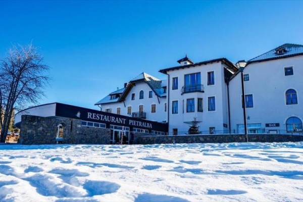 Sněhem pokryté náměstí před restaurací a budovou v zimním počasí.