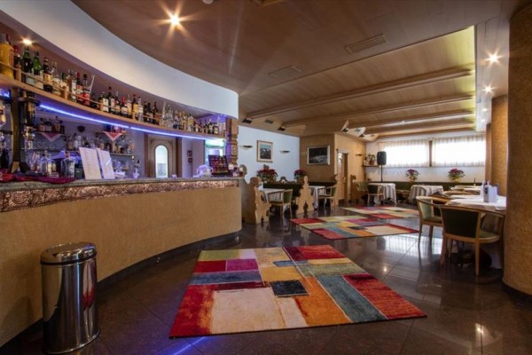 Interiér restaurace s barem, barevnými koberci a dřevěnými stoly se židlemi.