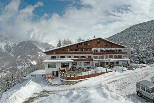 Horský hotel obklopený zasněženými horami a stromy.