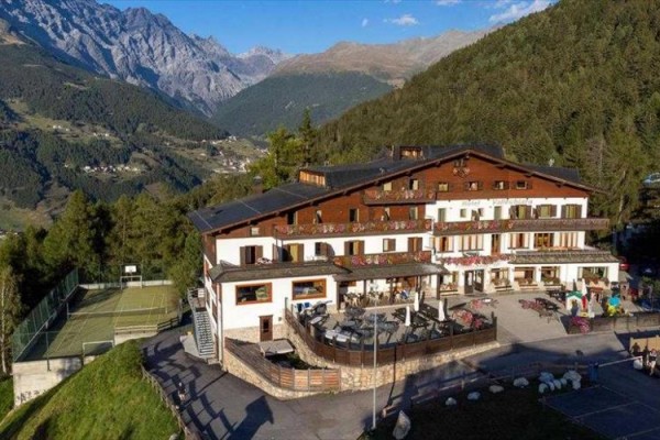 Horský hotel obklopený lesy a horami s tenisovým kurtem vedle.