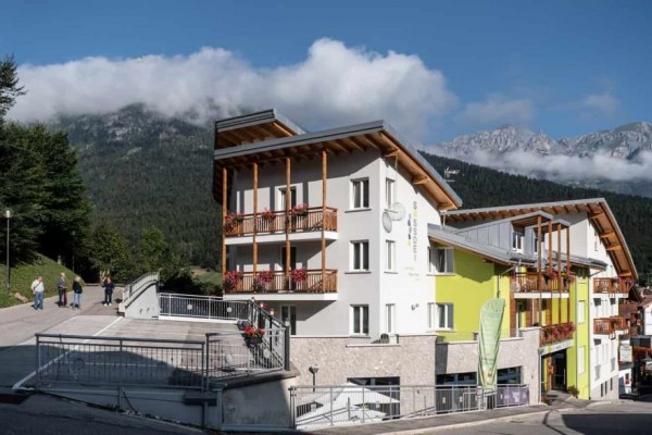 Moderní hotel v horské krajině s modrou oblohou a oblaky.