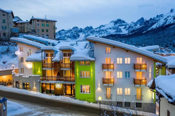 Moderní hotel se zasněženou střechou na pozadí horského panoramatu.