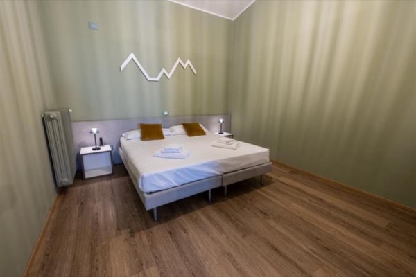 Moderní ložnice s manželskou postelí, dvěma lampičkami a dekorací na zdi.