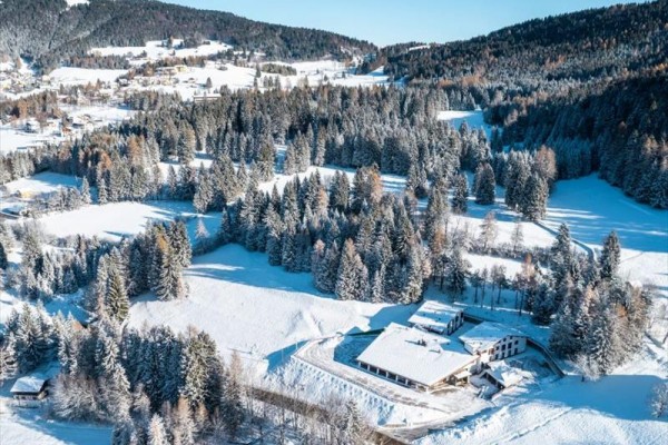 Zasněžená krajina s lesy a kopci pod modrou oblohou.