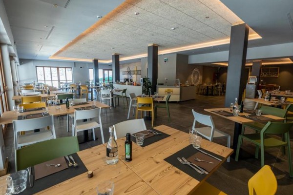 Moderní restaurace s dřevěnými stoly, barevnými židlemi a minimalistickým designovým osvětlením.