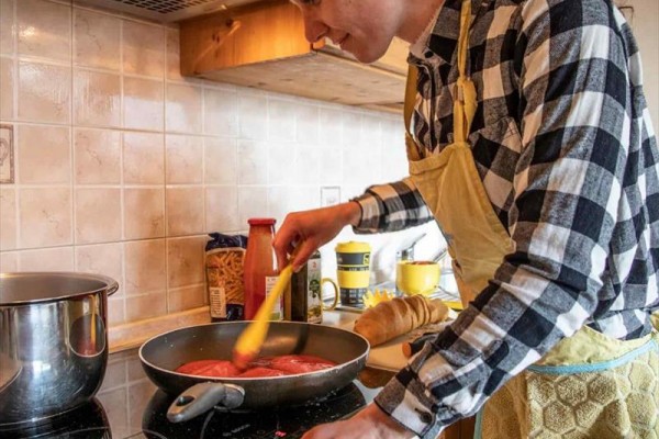 Osoba míchající rajčatovou omáčku na pánvi v kuchyni.