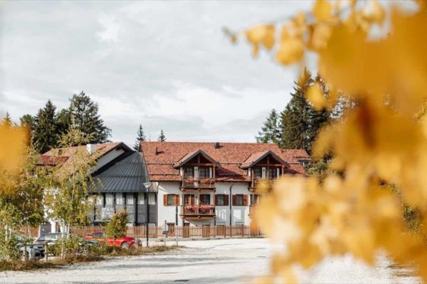 Budova s červenou střechou obklopená podzimními stromy.