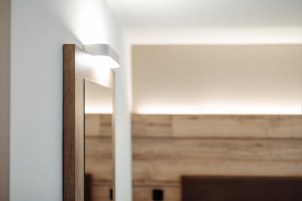 Dřevěný rám zrcadla a moderní nástěnná lampa v interiéru pokoje.