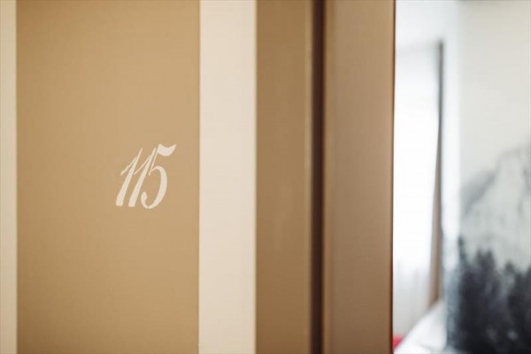 Číslo 115 na béžové zdi u dveří do pokoje.