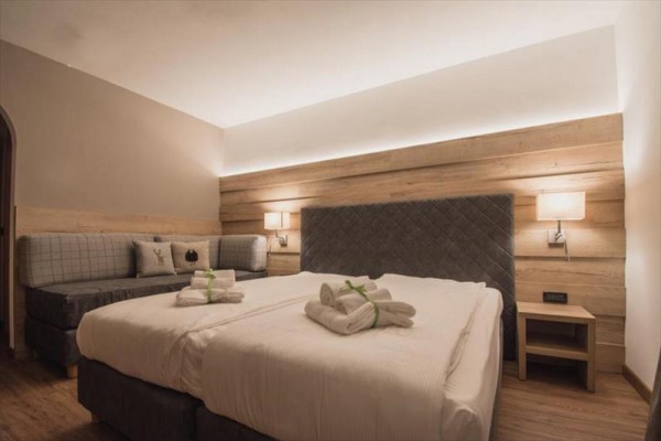 Moderní hotelový pokoj s dvoulůžkem a pohovkou, dekorován dřevěnými prvky.