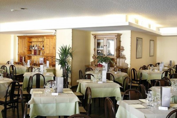 Restaurace se stolky pokrytými bílými ubrusy a zelenými prostíráními, připravená k obsluze.