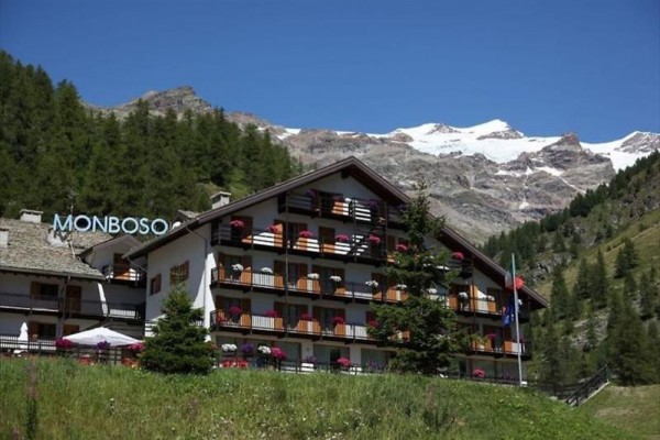Horský hotel s balkonovou výzdobou květin, obklopený lesy a horami.