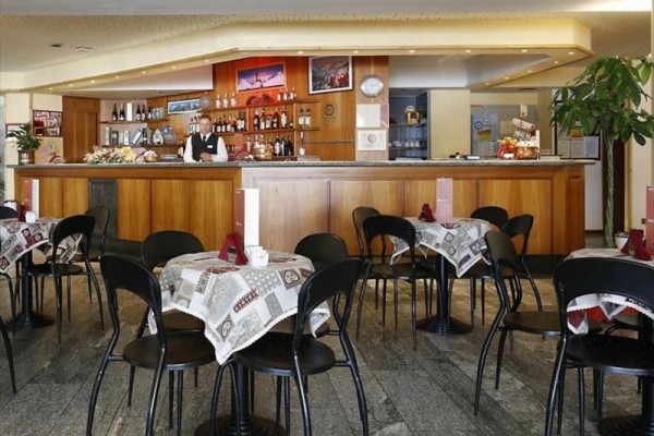 Bar s dřevěným pultem a stolem s ubrusy, kolem kterých je několik židlí.