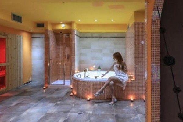 Wellness místnost s vířivkou a infrasaunou, kde sedí žena v bílém ručníku.