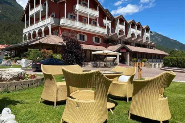 Hotel s červenou fasádou a ratanovým nábytkem na trávníku v popředí, obklopený horami.