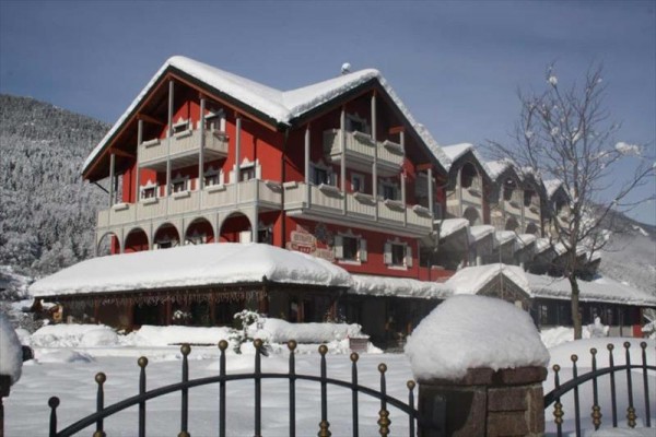 Červený horský hotel obklopený sněhem s horami v pozadí.  