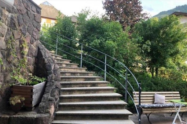 Křivolaké kamenné schody vedoucí nahoru mezi zelenými keři, vedle lavička a stolek.