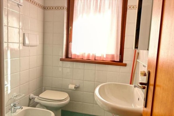 Koupelna s umyvadlem, toaletou a oknem s bílými závěsy.