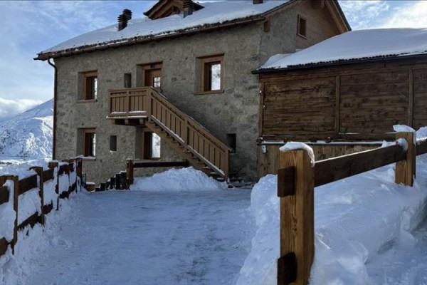 Kamenný dům se zasněženou střechou a dřevěným zábradlím v horské oblasti.