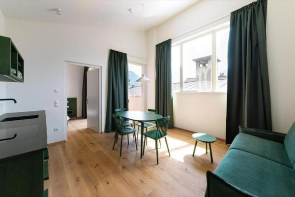 Moderní světlý obývací pokoj s tmavě zeleným nábytkem a dřevěnou podlahou.  