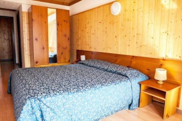 Pokoj s dřevěným obložením, manželskou postelí a šatní skříní.