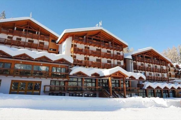 Velký horský hotel s dřevěnými balkony pokrytý sněhem za slunečného dne.
