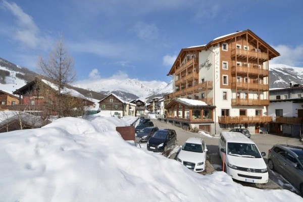 Dřevěný hotel ve zasněžené horské vesnici s řadou zaparkovaných aut.