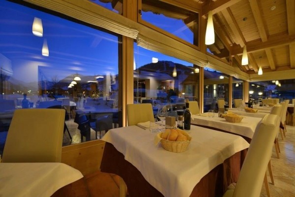 Interiér restaurace s prostřenými stoly a panoramatickými okny během soumraku.